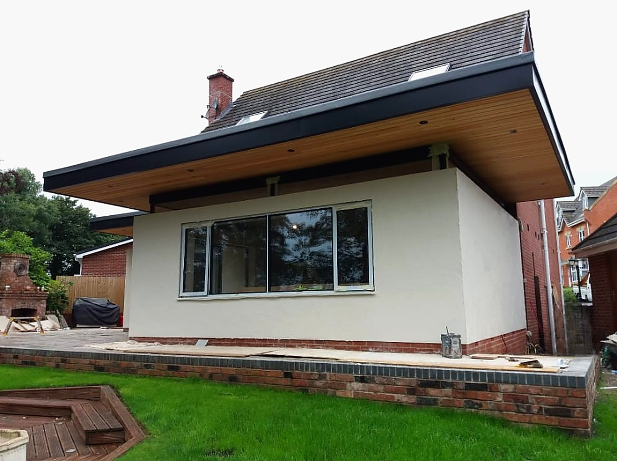 Rendered single storey extension with a deep overhanging flat roof and timber soffit