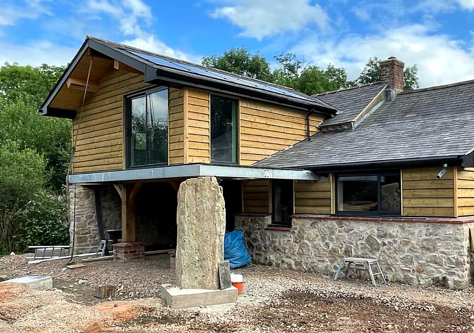 Timber clad first floor extension with solar panels above a stone cottage
