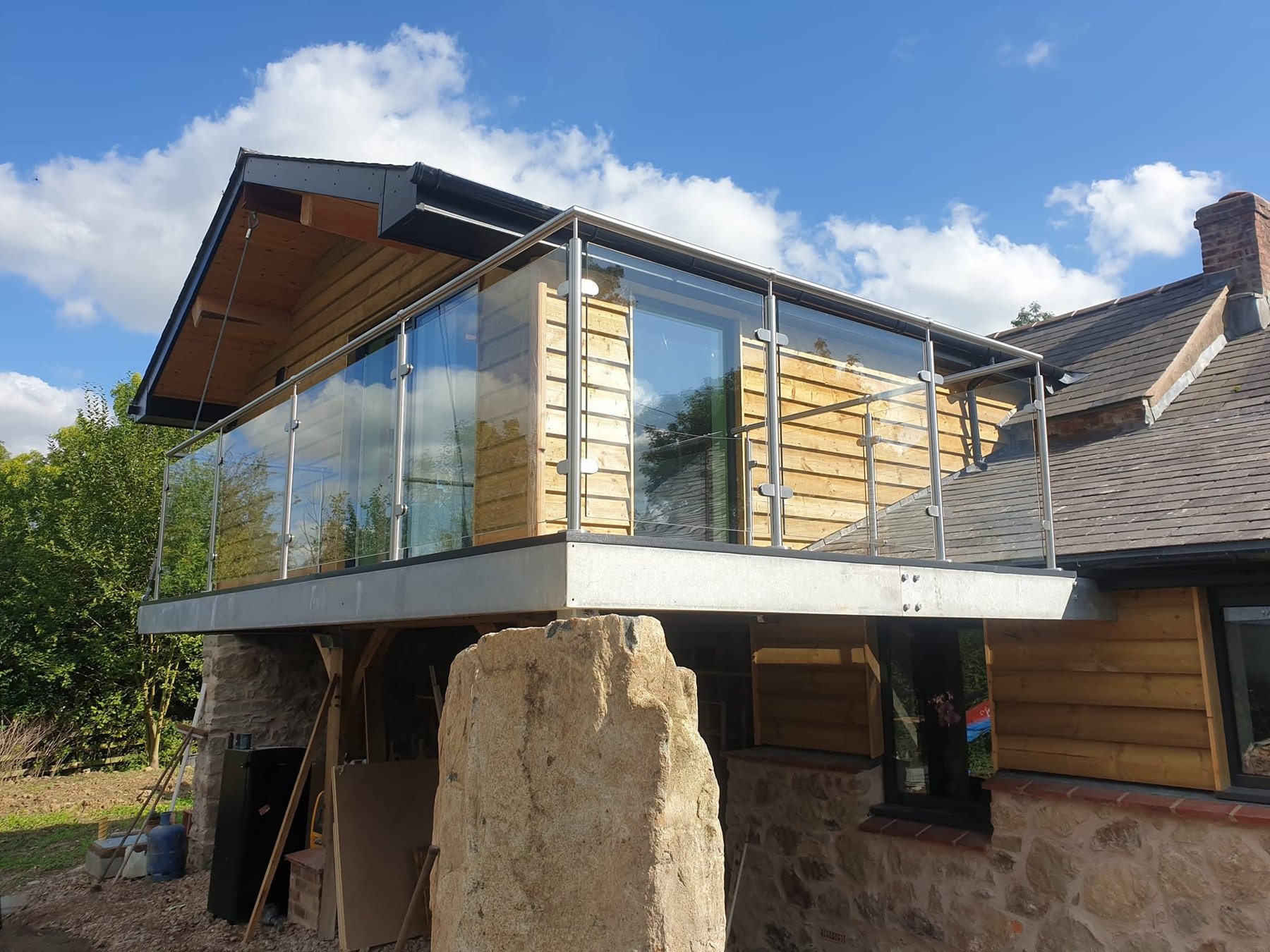 Timber clad extension with glass balcony above a stone cottage