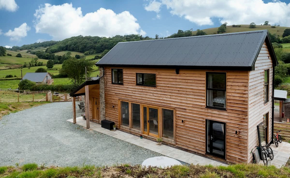 Two storey timber clad new build with a dark corrugated roof in open countryside